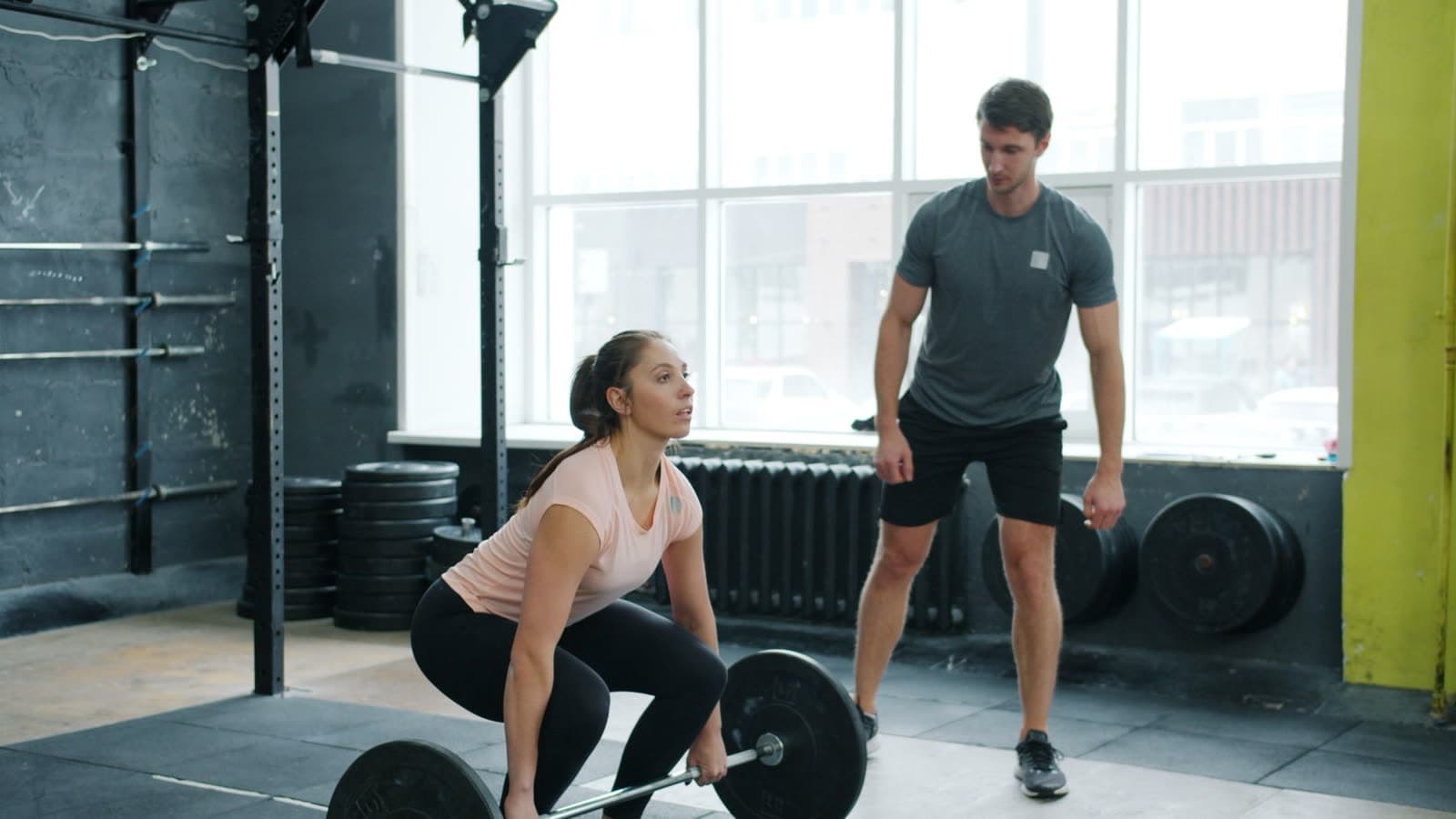 A coach watching a woman's deadlift form in the gym